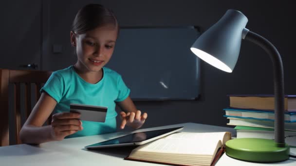 Niño usando tarjeta de crédito y tableta PC en la noche. Niño sonriendo a la cámara y le da a usted — Vídeo de stock