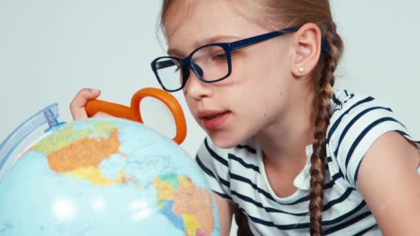 Close-up van schattige schoolmeisje portret bestuderen van de kaart van de wereld met hulp van school wereld door een vergrootglas — Stockvideo