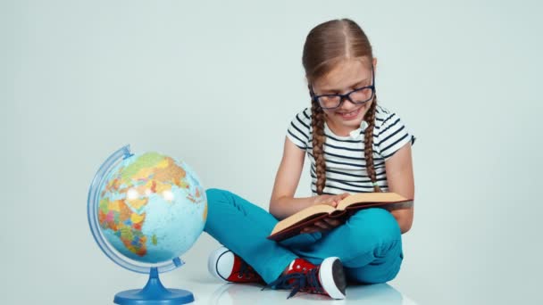 Gros plan portrait fille lecture livre et regarder caméra sur blanc près de l'école globe — Video