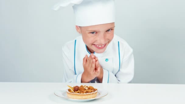 Close up retrato cozinheiro pequeno chef feliz esfrega as mãos e olhando para o bolo com nozes e sorrindo para a câmera — Vídeo de Stock