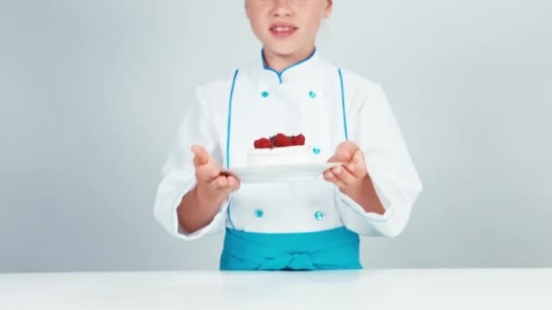 Close up portrait little chef baker holds meringue cake sniffing it and gives it you. Child smiling at camera — Stock Video