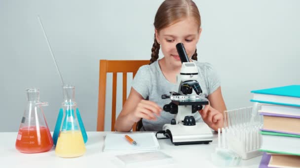 Nahaufnahme Porträt Schulmädchen mit Mikroskop und etwas Schriftzug in ihrem Schulheft — Stockvideo