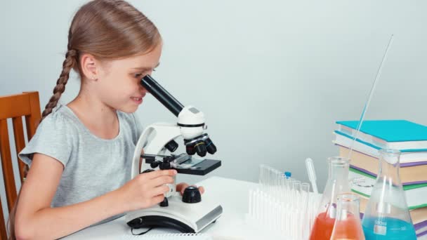 Primer plano retrato colegiala niño 7-8 años usando microscopio y mirando con sonrisa a la cámara. Pulgar hacia arriba. Panorama — Vídeos de Stock