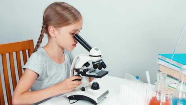 Bliska portret uczennica dziecko 7-8 lat za pomocą mikroskopu i uśmiecha się do kamery. Na białym tle — Wideo stockowe