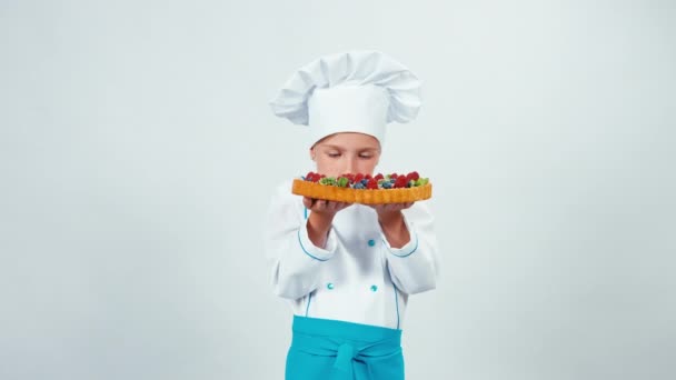 Close up ritratto giovane panettiere tenendo in mano torta al cioccolato con dolci e frutta annusandolo e sorridendo alla fotocamera con i denti. Isolato su bianco — Video Stock