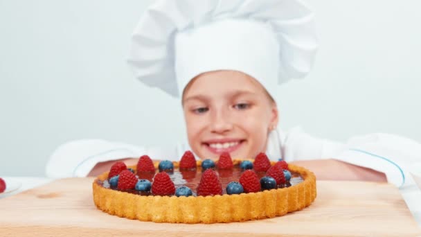 Primer plano retrato joven panadero mirando pastel de chocolate con frutas frambuesas y arándanos aislados en blanco — Vídeos de Stock