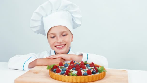 Close up retrato jovem padeiro perto de bolo de chocolate com doces e frutas. Isolado em branco — Vídeo de Stock