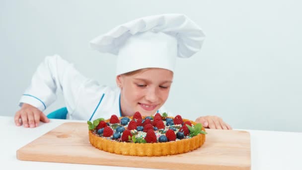 Close up portrait young chef baker examines chocolate cake with sweets and fruits. Isolated on white — Stock Video