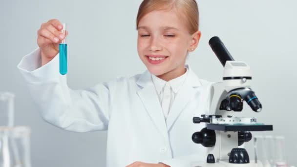 Close up retrato jovem estudante de química 7-8 anos segurando tubo de teste com produtos químicos azuis. Isolado em branco. Panning — Vídeo de Stock