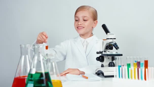 De cerca retrato joven farmacia escuela chica sosteniendo tubo de ensayo con productos químicos rojos y mirando a la cámara con sonrisa — Vídeos de Stock