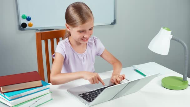 Симпатичная девочка-студентка лет 7-8 что-то смотрит на ноутбук, закрывает компьютер и улыбается перед камерой — стоковое видео
