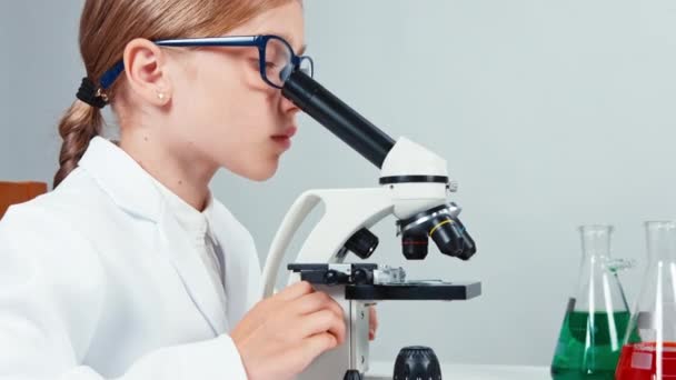 Extreme close up portrait young chemist school girl 7-8 years in glasses using microscope. Isolated — Stock Video