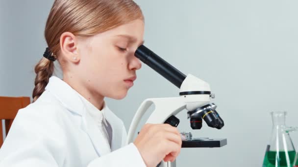 Extrém közelről portré fiatal kémikus iskolás lány 7-8 év mikroszkóppal. Mosolyogva kamera — Stock videók