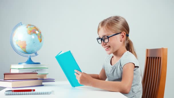 Chica de cuatro ojos leyendo su libro de texto y sonriendo a la cámara — Vídeos de Stock