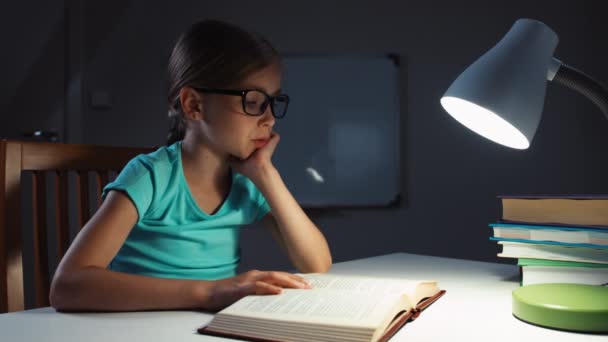 Κορίτσι διαβάζοντας ένα βιβλίο τη νύχτα στο σκοτάδι. Μαθήτρια 7-8 χρόνια χασμουρητά και αποκοιμιέται — Αρχείο Βίντεο