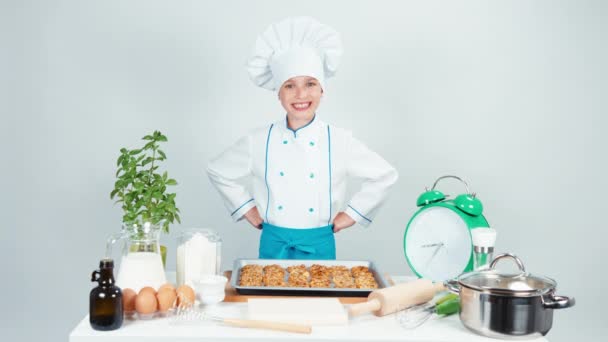 Gelukkig chef-kok koken meisje kind 7-8 jaar oud heeft bakken dienblad met koekjes en glimlachend in de camera. Geïsoleerd op wit. Duim omhoog. OK — Stockvideo