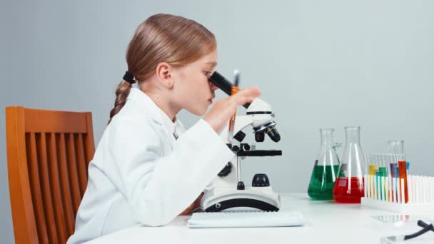 Χημικός ευτυχισμένη κοριτσάκι χρησιμοποιώντας μικροσκόπιο και να χαμογελά στη φωτογραφική μηχανή — Αρχείο Βίντεο