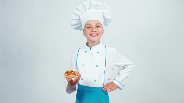 Felice panettiere carino entra nel telaio con piccola torta con noci e te lo dà. Chef 7-8 anni sorridente alla macchina fotografica. Isolato su bianco — Video Stock