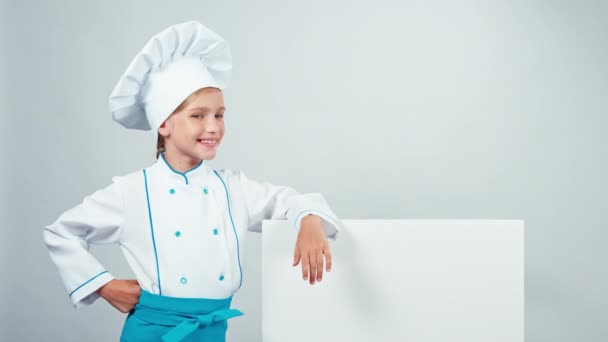 Piccolo cuoco cuoco in berretto in piedi vicino alla lavagna isolata su bianco guardando la fotocamera con i denti — Video Stock