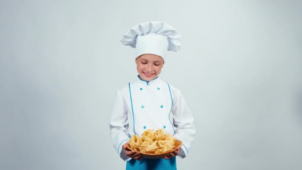 Pequeno chef dá-lhe massas de pé no fundo branco sorrindo para a câmera — Vídeo de Stock
