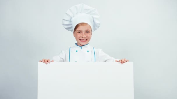 Pequeno cozinheiro chef bonito apontando dedo para quadro branco e sorrindo com dentes — Vídeo de Stock
