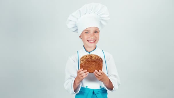 Portrait baker holds loaf of black bread in her hands and gives you and smiling at camera isolated on white background — Stock Video