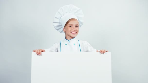 Retrato pequeño cocinero lindo en gorra con tablero blanco aislado en blanco sonriendo a la cámara con dientes. Pulgar hacia arriba. Ok. — Vídeo de stock