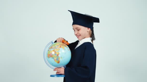 Portrait graduate girl 7-8 years in the mantle looking through magnifying glass globe on white — Stock Video