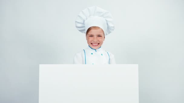 Portret lachen weinig chef kok in cap met wit bord geïsoleerd op een witte kijken naar camera — Stockvideo