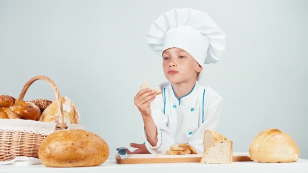 Portret kleine Bakker in de buurt van haar mandje eten van boterham geïsoleerd op witte achtergrond — Stockvideo