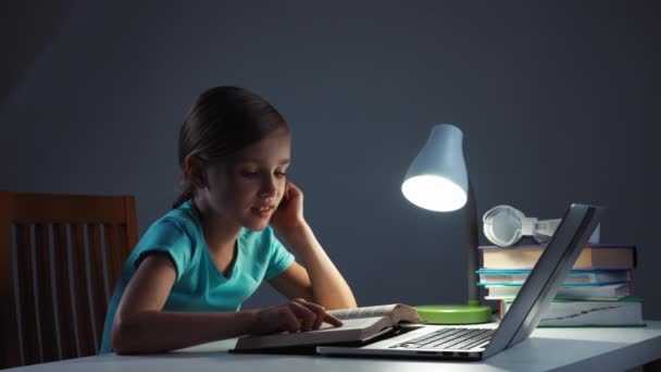Portrét školy dívka 7-8 let čtení učebnice v jejím stole v noci. Dítě se usmívá na kameru — Stock video