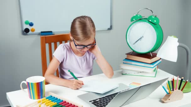 Portret schoolmeisje 7-8 jaar oud in brillen iets schrijven in de laptop en lachend op camera met tanden — Stockvideo