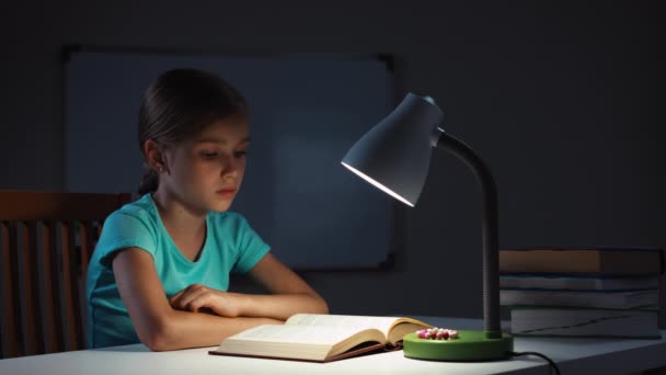Портрет школьницы, читающей книгу ночью в темноте и улыбающейся — стоковое видео