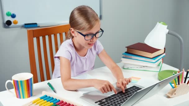 Retrato estudiante niña 7-8 años utilizando el ordenador portátil y regocijo. Niña sentada en su escritorio en el dormitorio — Vídeos de Stock