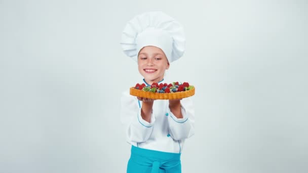 Retrato jovem padeiro segurando em sua mão bolo de chocolate com doces e frutas e sorrindo para a câmera com dentes. Isolado em branco — Vídeo de Stock