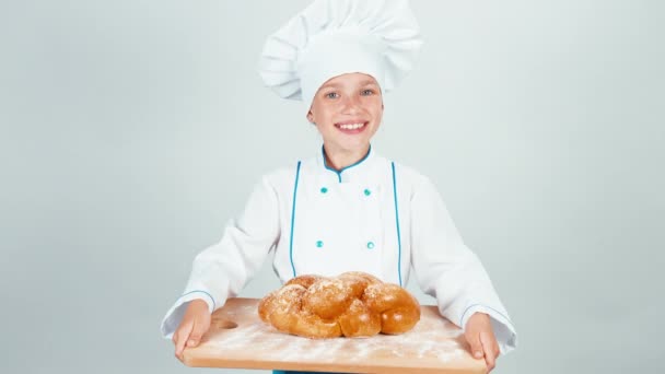 Retrato panadero joven sostiene tabla de cortar con pan trenzado y le da pan a la cámara y sonriendo aislado sobre fondo blanco — Vídeos de Stock