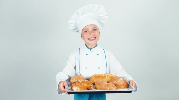 Retrato panadero joven sostiene horno-bandeja con pasteles y le da a la cámara y sonriendo aislado sobre fondo blanco — Vídeos de Stock