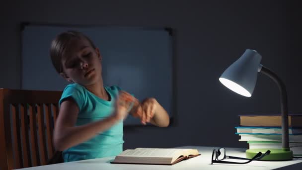 Escola menina 7-8 anos acorda na noite em sua mesa e lendo um livro — Vídeo de Stock