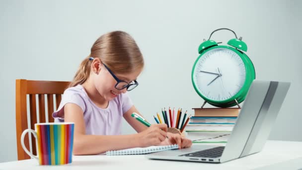 Skolan flicka barn 7-8 år gammal gör läxor med hjälp av bärbar dator. Ler mot kameran med tänder. Tummen upp. Okej — Stockvideo