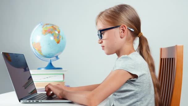 Chica de la escuela de cuatro ojos escribiendo en su computadora portátil sentado en el escritorio aislado sobre fondo blanco — Vídeos de Stock