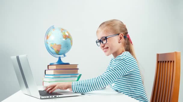 Colegiala usando laptop y escribiendo en cuaderno. Niña aislada sobre fondo blanco — Vídeos de Stock