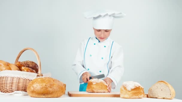 Молодая пекарь девушка 7-8 лет резки буханку хлеба и дает вам один кусок на камеру изолированы на белом фоне — стоковое видео