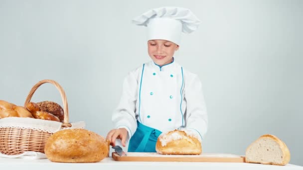 Молодая пекарь девочка 7-8 лет резки буханку хлеба изолированы на белом — стоковое видео