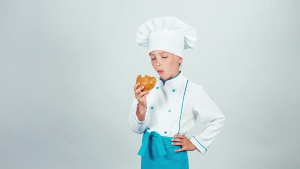 Junges Bäckermädchen isst kleines Brot und schaut in die Kamera, isoliert auf weiß — Stockvideo