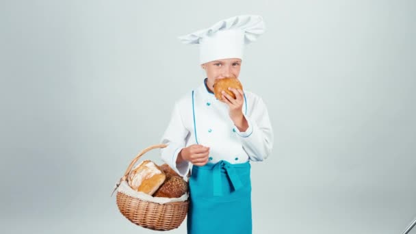 Молодая девушка пекарь держит корзину с хлебом и есть маленький хлеб улыбаясь в камеру изолированы на белом — стоковое видео