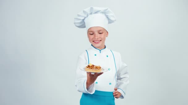 Il panettiere giovane tiene il piatto con piccola torta con noci e te lo dà. Chef 7-8 anni in piedi isolato su bianco — Video Stock