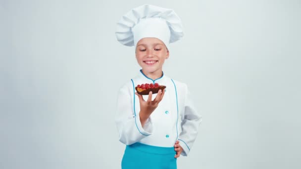 Молодой пекарь держит бисквит с малиной, стоящей изолированно на белом фоне. Пальцем вверх. Хорошо. — стоковое видео