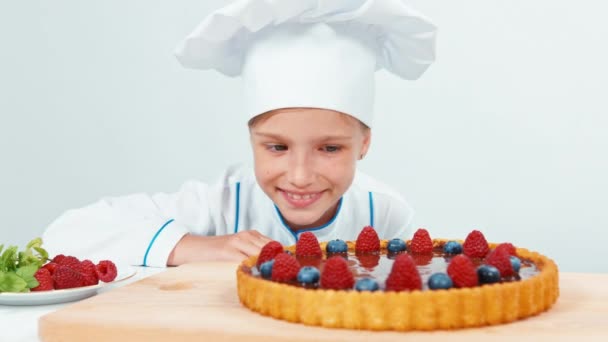 Mladí baker pohledu na čokoládový dort s ovocem maliny a borůvky izolované na bílém. Pohled na plochu — Stock video