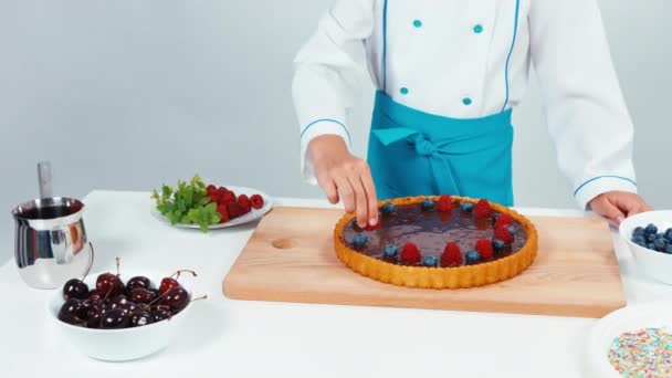 Νεαρός σεφ baker διακόσμηση κέικ σοκολάτας με βατόμουρα φρούτα απομονωμένα σε λευκό. Το Top view — Αρχείο Βίντεο
