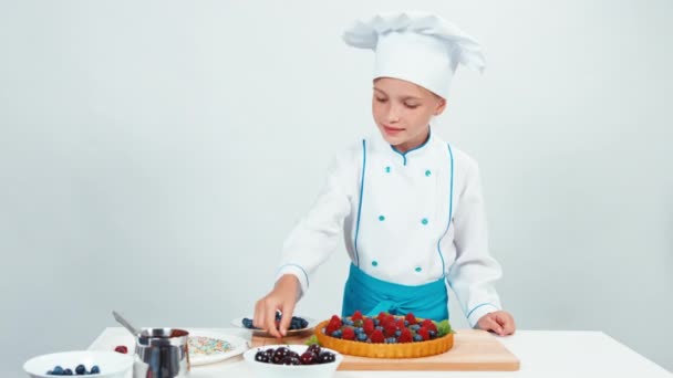 Cocinero joven decoración pastel de chocolate con dulces verdes y frutas. Aislado sobre blanco — Vídeo de stock